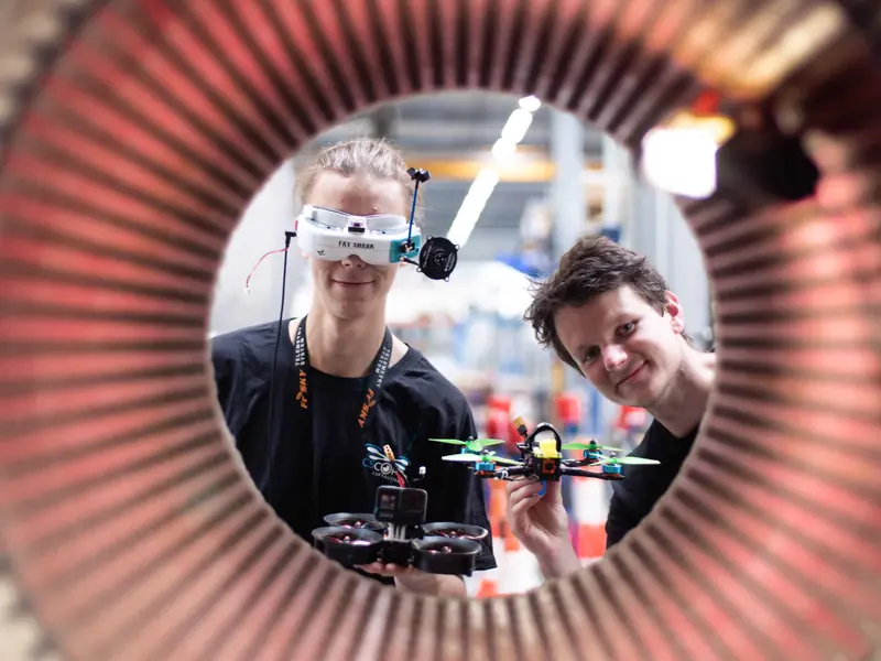 Zwei FPV-Piloten mit Drohnen in einer Produktionshalle, fotografiert durch einen Elektromotor-Stator
