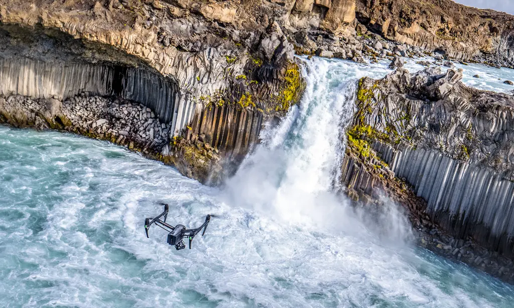 Kameradrohne über einem tosenden Wasserfall zwischen Basaltsäulen in Island